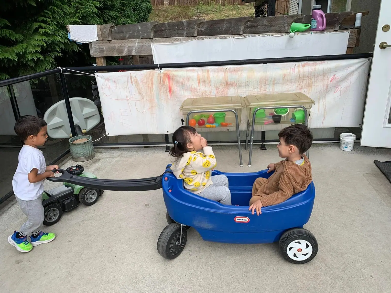 Two toddlers sitting together in a blue wagon on the centre's covered deck