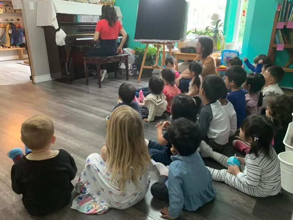 Children sitting on the floor listening to an educator play the piano